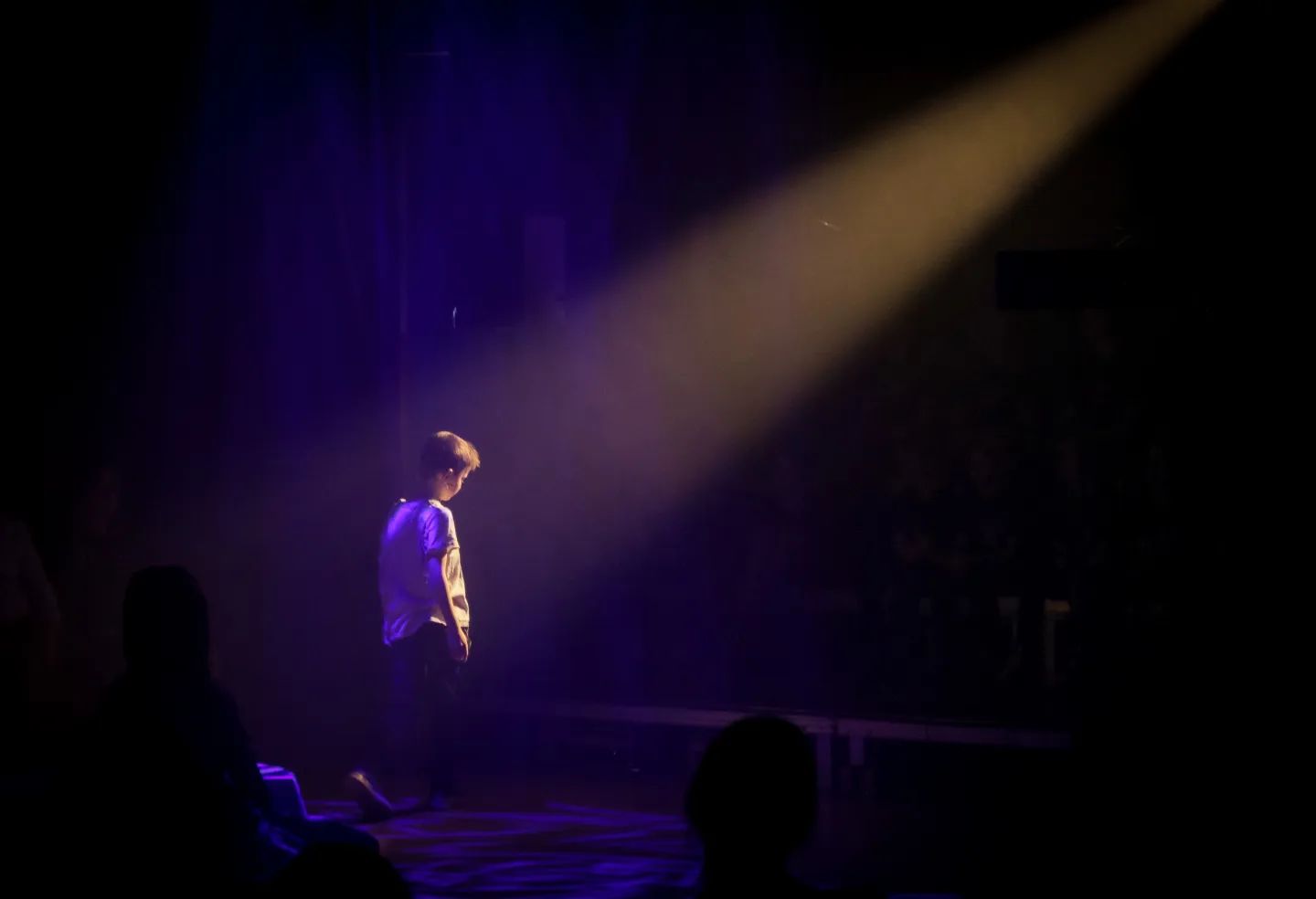 Ein Kind während eines Kindermusikals in einem Lichtbeam, ansonsten ist der Raum dunkel